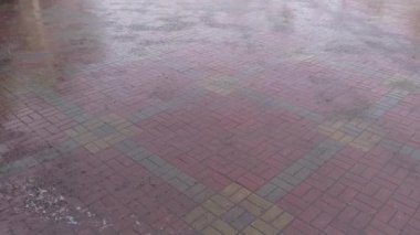 Bir kiremit kaldırıma sağanak yağmur yağıyor. Boş şehir caddesinde yağmurlu bir hava, yerde akan sular büyük su birikintilerine karışıyor.
