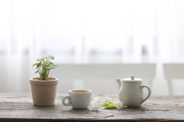 Beyaz çay fincanı ve çaydanlık. Ahşap masa iç kısımlarında bitki var.