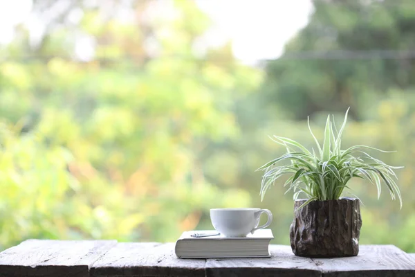 notebook and white coffee cup with plant in small wooden pot on wooden table at outside