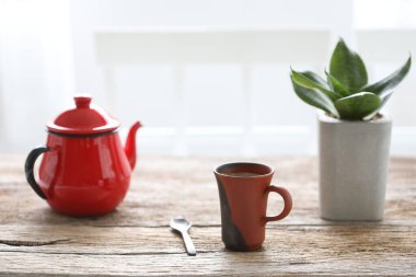 Kahverengi ahşap masa üzerinde yılan bitkisi olan kırmızı çay fincanı ve çaydanlık