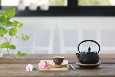 Siyah geleneksel çay fincanı ve ahşap masa üzerinde pembe çiçek.