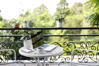 Kahve fincanlı dizüstü bilgisayar, saksı ve balkondaki metal masaya dizüstü bilgisayar.