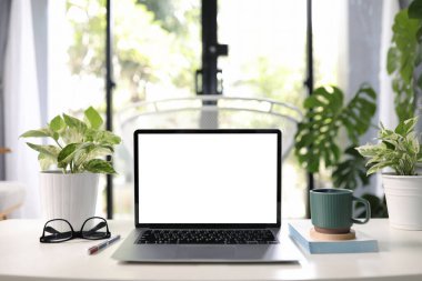 Yeşil kahve fincanı, kitap ve güneş gözlüğü konforlu ev ofisi olan beyaz, boş ekranlı bir laptop. 