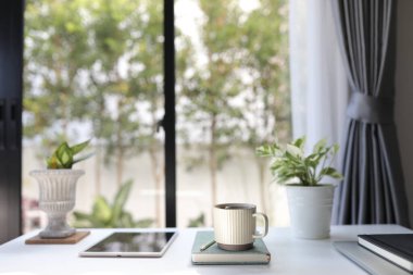 Tabletli seramik kahve fincanı ve beyaz masadaki not defterleriyle birlikte demlik. 