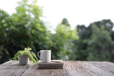 Beyaz kahve fincanı ve kahverengi ahşap masa üzerinde bitkiler olan defterler.