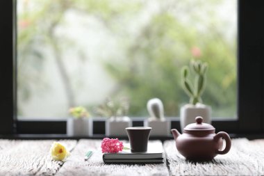 Çaydanlıklı çay fincanı ve pencerenin önünde kaktüs bitkisi olan eski kahverengi masadaki çiçekli defterler. 