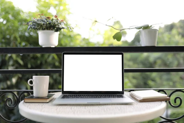 Laptop with coffee cup and plant pots with notebooks on metal table at balcony outdoor