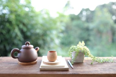 Oryantal kahverengi çaydanlık, ahşap bardak ve küçük yeşil saksıyla süslenmiş defter kalem. 