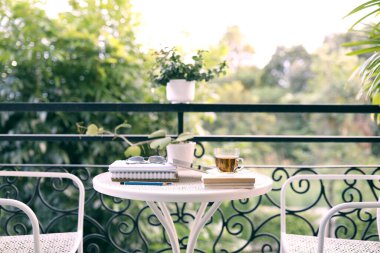 Çay fincanı, defterler, bardaklar ve koridordaki beyaz metal masaya saksı. 