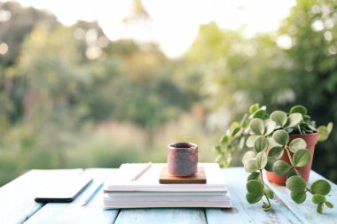 Mavi ahşap masada, üzerinde defter ve telefon olan taştan bir bardak.