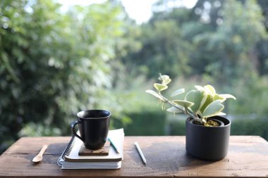 Siyah kahve fincanı ve eski kahverengi ahşap masa üzerinde defter ve kalemle demlik.