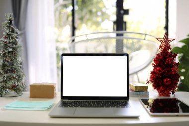 Tabletli ve maskeli dizüstü bilgisayar evden alınmış minyatür Noel ağacı işleriyle süslenmiş.
