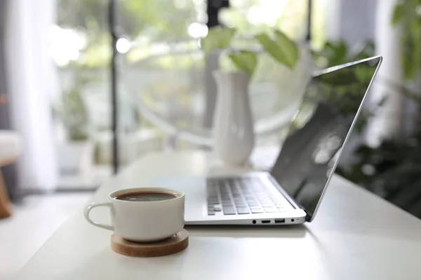 Laptop and coffee cup and plant pot on wooden table in front of windows glass door