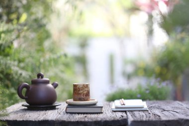 Kahverengi bambu kabı, Asyalı kil çaydanlığı ve ahşap masa üzerinde not defterleri.