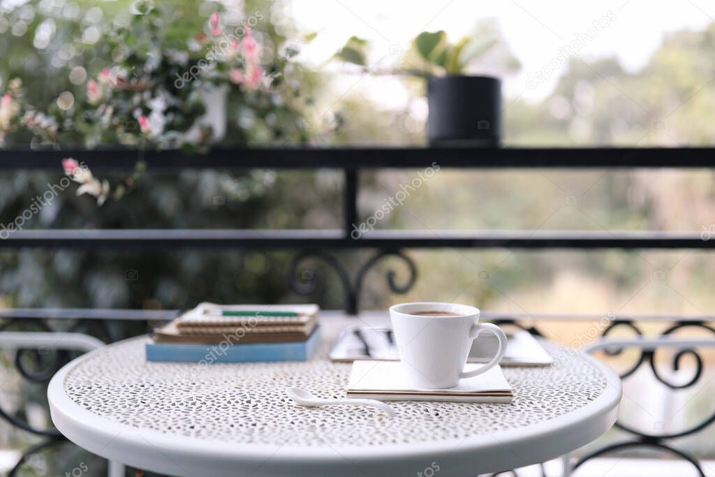 White coffee cup and notebooks on vintage metal table at balcony