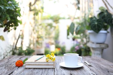 Beyaz seramik bardak ve kasımpatı ve ahşap masadaki gül çiçekli defterler.