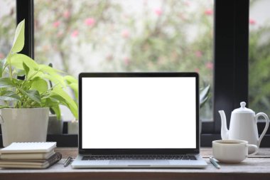 Beyaz ekran dizüstü bilgisayar, kahve fincanı, defter ve saksı.