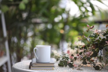 Beyaz kahve fincanı ve beyaz metal masada saksı olan bir defter.