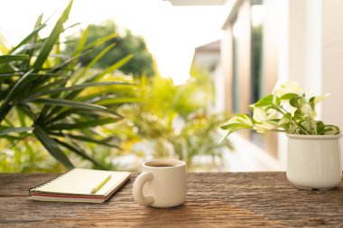 White coffee cup and notebook, old wooden table, at balcony outdoor