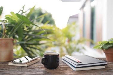 Sade kahve fincanı, telefon ve defter, ahşap masa, açık hava yazıları.