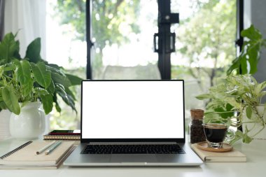 Dizüstü bilgisayar, kahve bardağı ve saksı masa örtüsü çalışma alanına yerleştirilmiş.