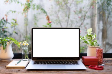 Dizüstü bilgisayar, kırmızı hediye kutusu ve makas pencerenin önündeki ahşap masada.