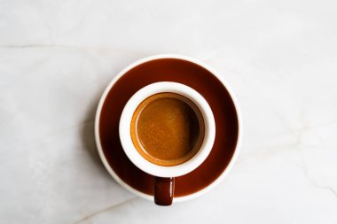 Kahverengi bir fincanda kahve, mermer yüzey masasının üzerinde düz bir şekilde yatıyordu.