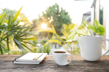 Beyaz kahve fincanı ve üzerinde çiçek desenleri olan bir yığın defter. Ahşap masa ve güneş ışığı arkaplanı.