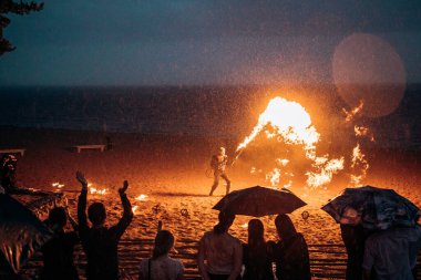 Şemsiyenin altında mezunlar, kumsalda alev makinesi olan bir adamın olduğu bir ateş gösterisi izliyorlar. Rusya, St. Petersburg, 08.08.2020.