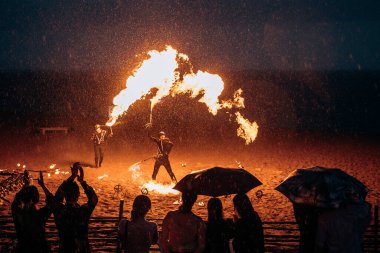 Şemsiyenin altında mezunlar, kumsalda alev makinesi olan bir adamın olduğu bir ateş gösterisi izliyorlar. Rusya, St. Petersburg, 08.08.2020.