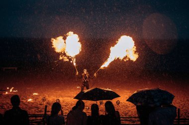 Şemsiyenin altında mezunlar, kumsalda alev makinesi olan bir adamın olduğu bir ateş gösterisi izliyorlar. Rusya, St. Petersburg, 08.08.2020.