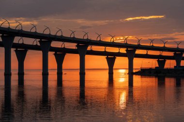 St. Petersburg 'daki Kanonersky Adası' nda yakıcı gün batımı. Batı yüksek hız çapı. Otomobil köprüsü. Finlandiya Körfezi. Turuncu gökyüzü ve sudaki yansıma