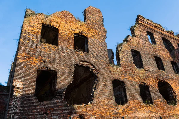 An old ruined building, without windows or doors, made of red bricks. The destroyed walls of the house.