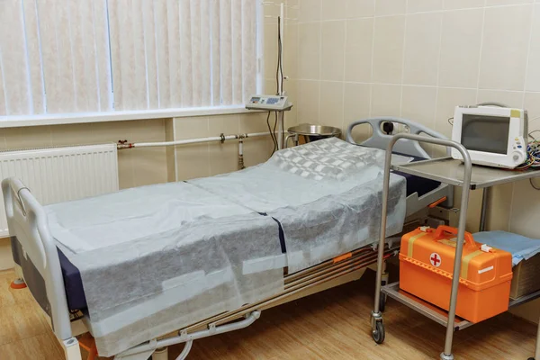 Emergency area in the clinic. Light sterile recovery room with bed. The light is on. Ambulance box. Medical equipment. Trolley for transporting patients