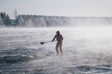 Dalgalara karşı kürek çeken kırmızı dalgıç kıyafetli bir sörfçü. Vuoksa nehrinde kış yemeği sörfü. Akıntıyı kaybet