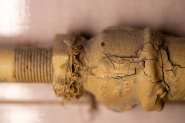 Dairedeki metal bir su borusunda eski sarı boya. Boya çatlamış. Pas seçici odak noktası soyuluyor. Sarı boyanmış.