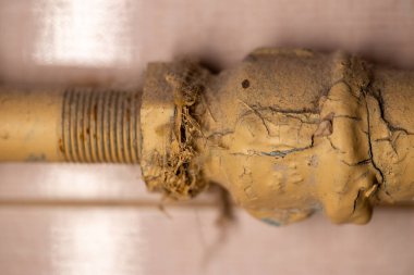 Dairedeki metal bir su borusunda eski sarı boya. Boya çatlamış. Pas seçici odak noktası soyuluyor. Sarı boyanmış.