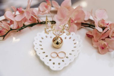 Düğün günü. Masadaki beyaz tabakta altın alyanslar, çiçek süslemeleri, düğünde resmi tören, yakın plan. Mutlu bir gün. Düğün anı, yıldönümü, nişan