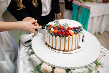Damat ve ağırlıksız adamlar meyve, ahududu, çilek ve yaban mersiniyle süslenmiş karamel ile sulanmış bir düğün pastası kestiler. Yakın plan. Tatil kavramı