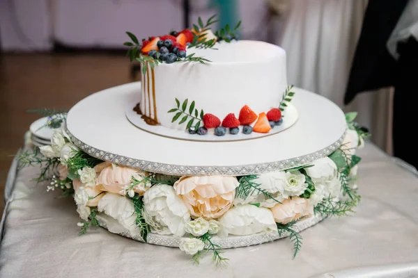 A beautiful wedding cake decorated with fruits, raspberries, strawberries and blueberries, watered with caramel. Confectionery on the table. Holiday concept