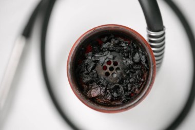 Kırmızı silikon kaplı beyaz tabakta nargile, sigara içtikten sonra yanmış meyve tütünü. Yakın plan.