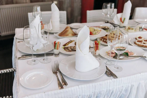 Establecimiento de mesa para un banquete o celebración. Vasos de vino vacíos para licores, champán y jugo. Pon la mesa. Servilletas de tela en bandeja. Sala de banquetes. Aperitivos fríos y ensaladas —  Fotos de Stock