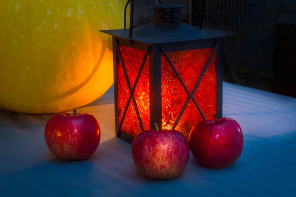Pumpkin and Red appleson Halloween in the warm light of the lanterns, carved pumpkin. Orange lantern candle. Simple Halloween still life.