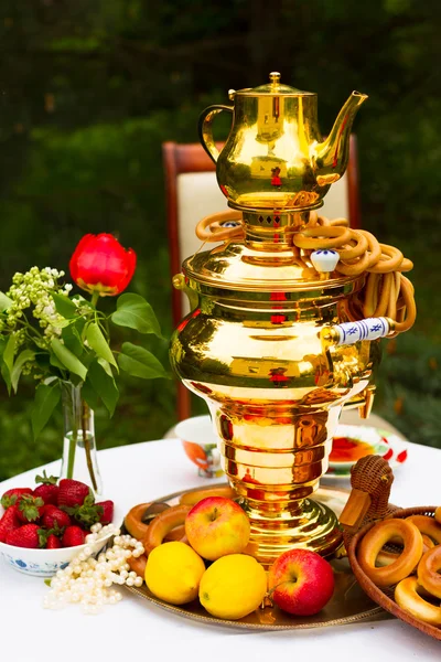 Русский самовар и чай, клубника на тарелке Гжель, лимоны, цветы, сушка и бублики — стоковое фото