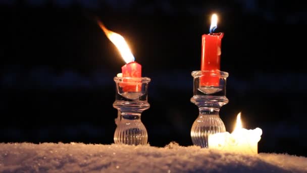 Rote Kerzen, Kristallleuchter und eine große Kerze stehen im Schnee und brennen. Es ist kalt und dunkel. Schnee sind die kleinen Schneeflocken, er fällt hart. das Gefühl von Winter, Urlaub, Weihnachten und Neujahr. — Stockvideo