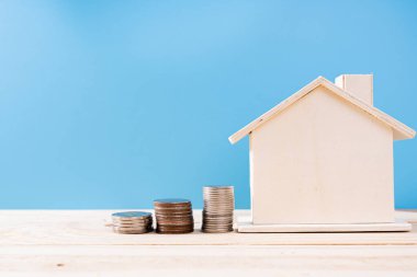 Yığınla bozuk parası olan ahşap ev, izole edilmiş mavi arka plan. Emlak yatırımı ve konut kredisi finansal konsepti.