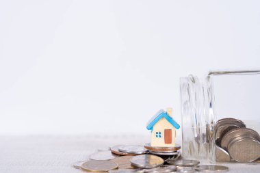 Kavanozdaki ev ve madeni paralar gri arka planda. Emlak yatırımı ve konut kredisi finansal konsepti.