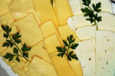 Bitkilerle süslenmiş bir tabakta ince dilimlere ayrılmış çeşitli peynir türleri. Hafif atıştırmalık olarak delikleri olan peynir..