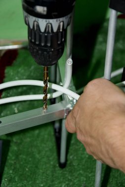 Yeşil arka planda, çeşitli yedek parçalarla çevrili bir adam alüminyum bir şeritte, antende matkapla matkaplar. Adam anten için delikler açıyor..