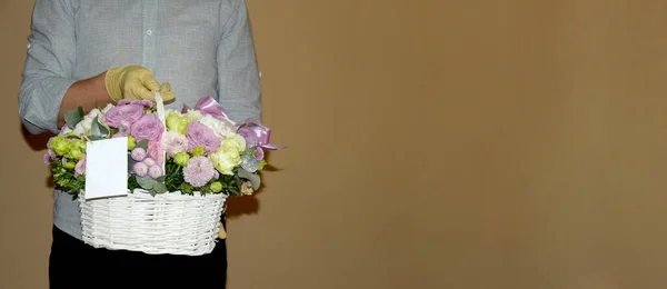 Un messager mâle livre un beau panier en osier avec des fleurs. Une main d'homme dans un gant tient un panier de roses et le donne à tout le monde. Beaucoup de place pour le texte. — Photo